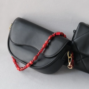 Macro detail of high-quality black leather saddle bag with distinctive red acrylic bead strap