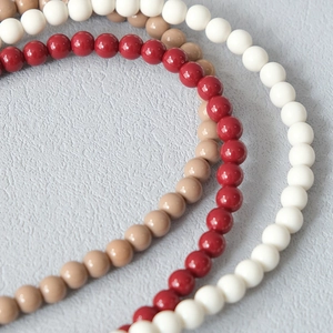 Détail de chaînes en perles acryliques rouges, beige et blanc crème avec fini brillant