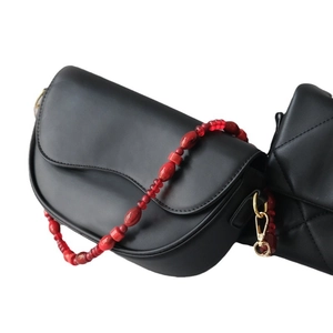 Classic black leather saddle bag featuring a bold red acrylic beaded shoulder strap accent