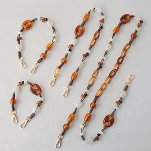 Detailed macro view of amber and frosted bead chains with golden lobster clasps for bags