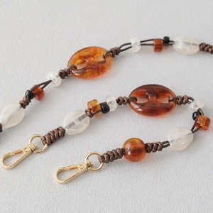 Detail of amber and white acrylic bead chain with golden metal spring hooks for handbags