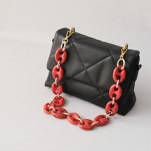 Détail de la grosse chaîne acrylique rouge marbré et crochet doré sur sac noir