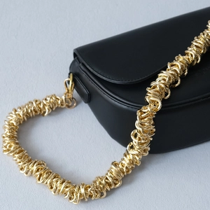 Détail d'un sac besace noir avec une bandoulière à gros maillons de chaîne dorés entrelacés