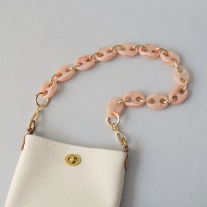 Détail d'un sac en cuir crème avec chaîne en résine rose et fermoir doré rotatif