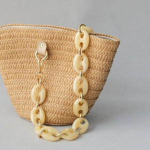 Détail de la chaîne en résine crème et du fermoir en métal doré sur un sac en paille