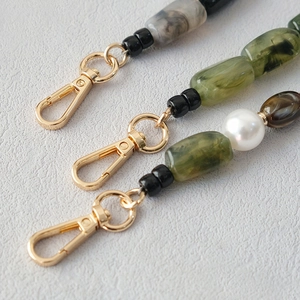 Detailed close-up of marble-patterned acrylic beads and golden lobster clasp on a bag strap