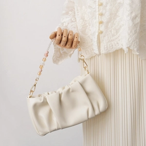 Detail of creative beaded strap with transparent and pastel beads on a white pleated bag