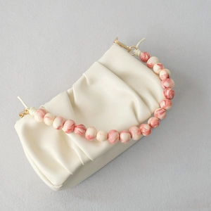 Close-up of white leather cloud bag with marbled acrylic bead handle and gold hardware