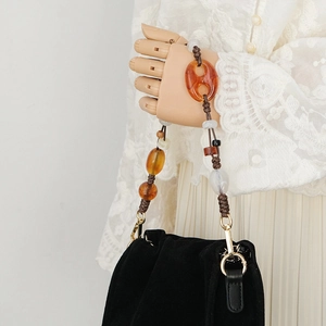 Detail of amber and cream resin bead bag strap with golden metal clasp on wood hand