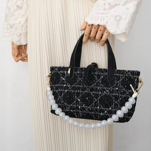 Detail of tweed handbag featuring classic geometric texture and oversized pearl strap
