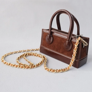 Detail of a brown leather and suede crossbody bag with a gold metal woven chain strap