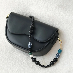 Close-up of a black crescent leather bag with unique multi-color acrylic beaded strap