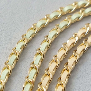 Close-up of golden metal chain woven with light mint green and beige leather straps