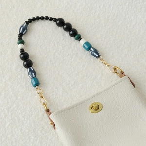 Detail of cream pebble leather bag with vintage beaded strap and gold turn-lock closure