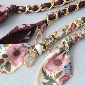 Detailed close-up of golden metal chains interwoven with floral silk scarf straps and hooks