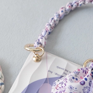 Detail of purple floral phone case featuring a woven fabric strap and metal clip