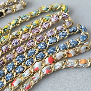 Detailed close-up of golden metal chains woven with various colorful floral silk scarves