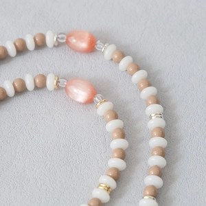 Detail of pink cat-eye stone beads with gold spacers and acrylic beads on a textured base