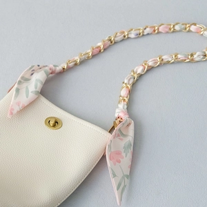 Close-up of cream leather bag with golden chain and floral scarf handle detail