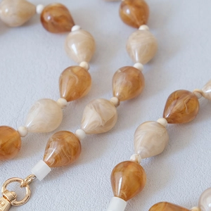 Macro shot of amber-textured resin water-drop beads with elegant gold metal clasp