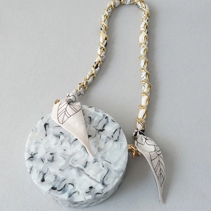 Detailed close-up of marble pattern round handbag with golden silk scarf chain strap