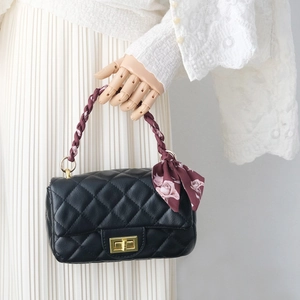Détail du sac à main en cuir noir matelassé avec poignée tressée rouge et foulard fleuri