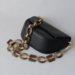 Detail view of black crescent crossbody bag with amber resin and gold chain strap