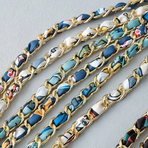 Detailed macro view of pale gold metal chain straps interwoven with colorful silk ribbons