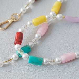 Detailed close-up of acrylic beads and pearls on phone strap with golden metal lobster clasp
