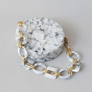 Detail of round marble resin clutch bag with chunky gold chain strap and acrylic links