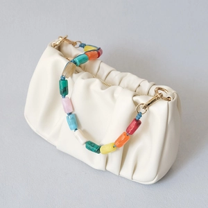Détail d'un sac à main plissé blanc crème avec une chaîne de perles en acrylique colorées