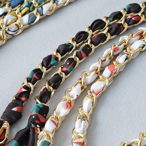 Detail of golden metal chain straps interwoven with floral print silk ribbons for handbags