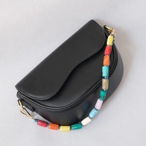 Détail de la bandoulière en perles acryliques colorées sur un sac de selle noir