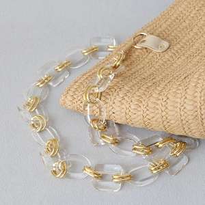 Chunky acrylic and gold metal chain strap on a woven straw bag accessory for women