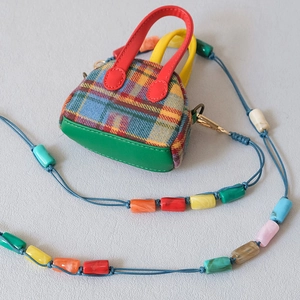 Détail de perles en résine colorées sur une bandoulière bleue avec mini sac à carreaux