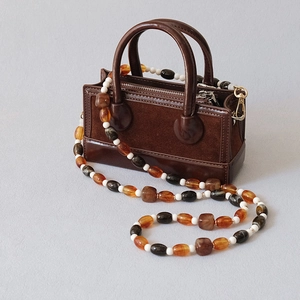 Détail d'un mini sac en cuir marron avec une bandoulière en perles acryliques colorées