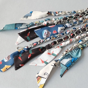 Detailed close-up of cartoon print silk scarf interwoven with silver metal bag chain straps