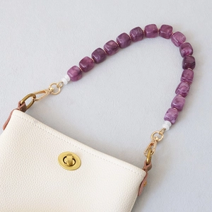 Detail of purple marble resin bead chain with gold metal clasps on a cream bag