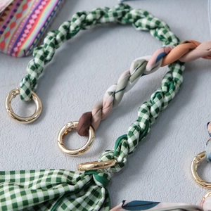 Detail of silk scarf handle straps with green plaid patterns and gold metal buckles