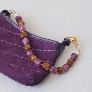 Detail of purple suede handbag featuring chunky resin chain link in amber and violet