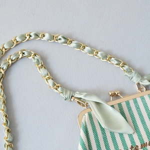 Detail of green striped fabric handbag with gold chain strap interwoven with silk ribbon