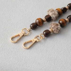 Detail of wooden beads strap with grey pompom and golden metal lobster clasps