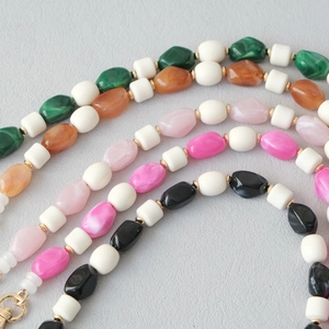 Détail de perles en acrylique colorées et chaîne en résine avec fermoir doré sur gris