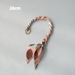 Close-up of a 26cm woven handbag chain with pink orange straps and a leaf print silk scarf