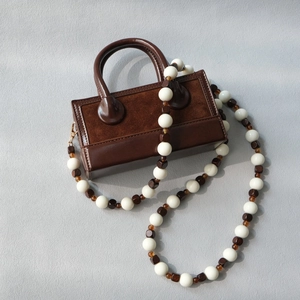 Detail of cross-body bag featuring decorative acrylic and wooden bead strap accessory