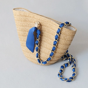 Detail of woven straw bucket bag with blue silk scarf wrapped on golden metal chain strap