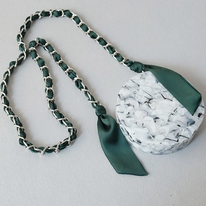 Macro shot of silver metal chain strap woven with dark green silk ribbon on marble purse