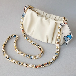 Close-up of cream pleated dumpling bag with gold chain and cat pattern silk scarf strap