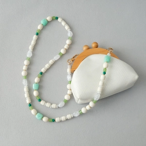 Détail de la bandoulière en perles acryliques et fermoir en bois sur un sac blanc
