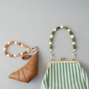 Détail des poignées en perles acryliques sur sac croissant marron et pochette à rayures